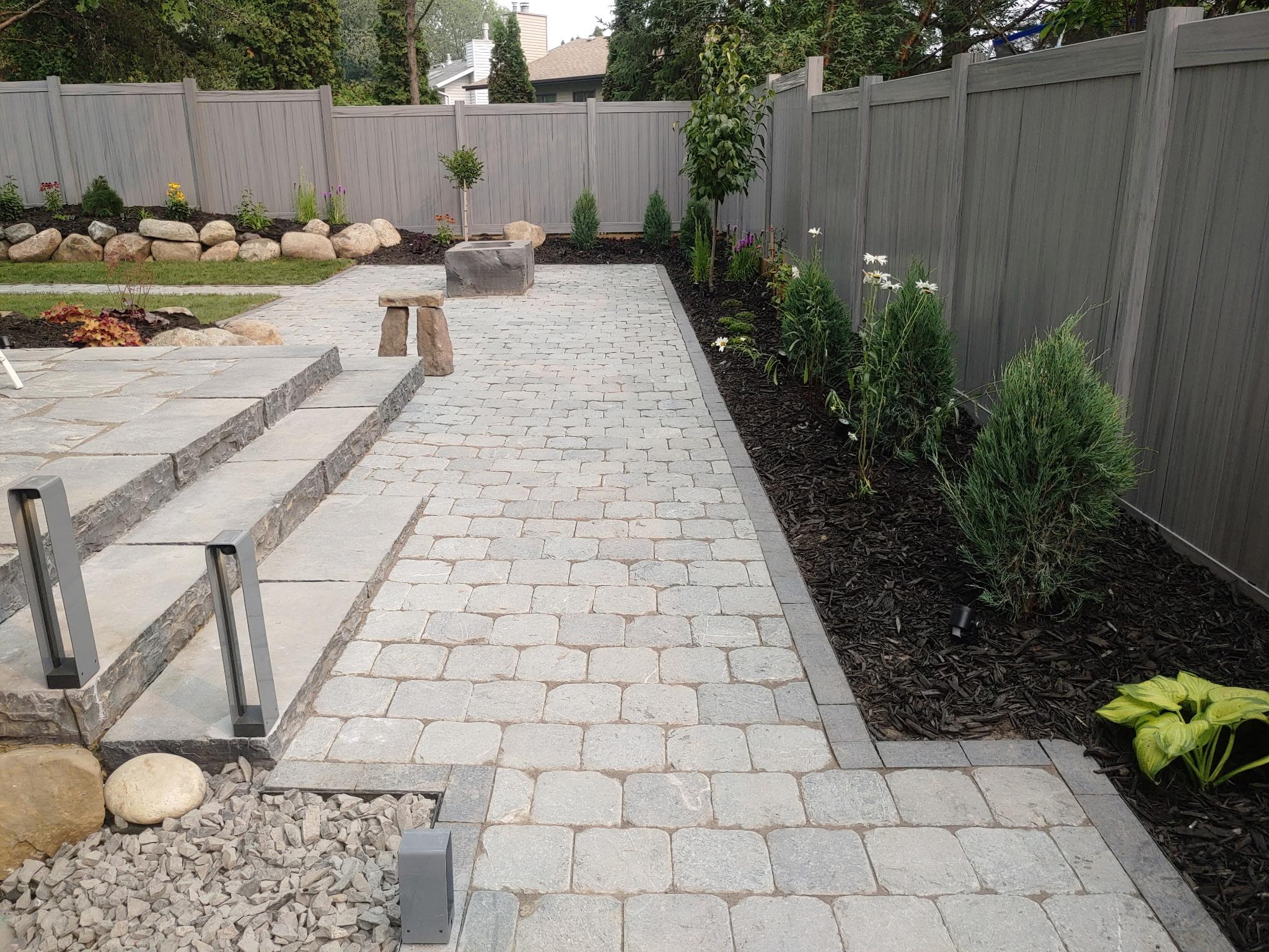 ALA Landscaping completed backyard paving stone pathway with layered planting beds and retaining wall